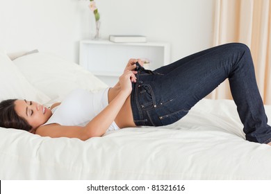 Pretty Woman Lying On Bed Trying To Close Her Jeans In Bedroom