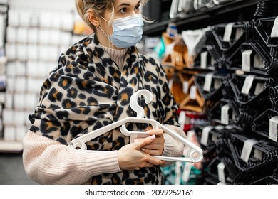 Pretty Woman In Medical Mask Thought About Choosing Set Of Plastic Hangers For Organizing Dressing Room Space In Shopping Center's Utility Department. New Normal Concept .Organization Of Storage.