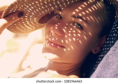 Pretty woman on the beach, closeup portrait of a nice female hides her face from the sun under a straw hat, skin protection, happy healthy summer vacation                               