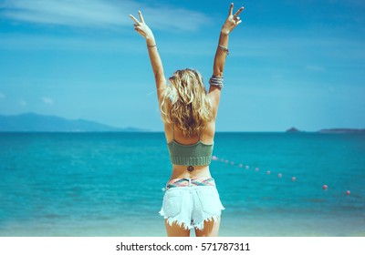 pretty woman posing in the sea, blue sky, hair wild, victory hand up!, outdoor portrait hipster, fashion model, pretty female, denim shorts, hippie, tattoo, hipster girl, Amsterdam, denim shorts,cute 