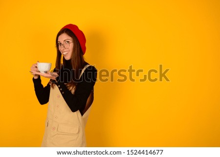 pretty woman in a red beret with glasses and a cup of coffee basks on a yellow background autumn october