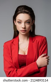 pretty woman in red blazer and earrings looking at camera isolated on grey
