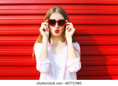 Pretty woman in red sunglasses blowing lips kiss over colorful background