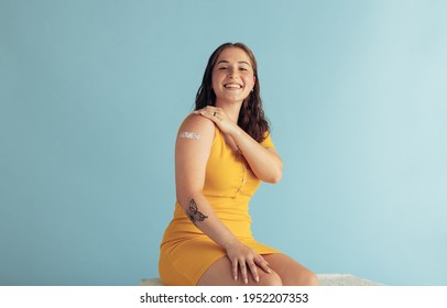 Pretty Woman Showing Her Arm After Getting Vaccine. Female With Band-aid On Her Arm After Receiving Flu Shot On Blue Background.