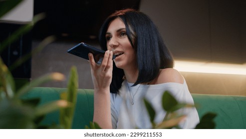 Pretty woman sit in kitchen hold smart phone talk on speakerphone. Female recording audio message for friends or parents, sharing news using mobile phone application. - Powered by Shutterstock