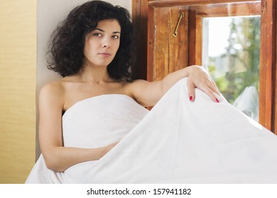 Pretty woman sit near window covered by bed blanket