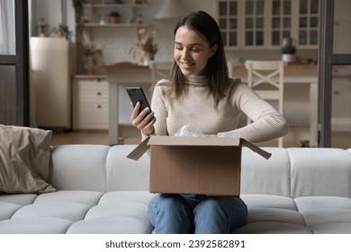 Pretty woman sit on sofa opens received courier parcel box, reviewing order in retail services using app on smart phone, check items feels happy with delivered goods. E-commerce client, tech concept