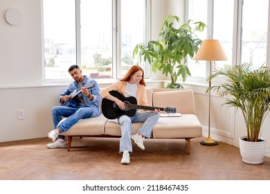 pretty woman sitting comfy sofa playing guitar learning spend time with man together stay home quarantine safety modern interior living room indoors, redhead lady and handsoem guy in casual wear - Powered by Shutterstock