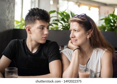 Pretty Woman Sitting With Her Teenage Son In A Cafe And Talking - Son Looking Lovingly At Mom. The Concept Of Communication Between Parents And Children