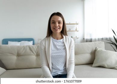 Pretty woman sitting on sofa in living room smile look at camera taking part videocall involved in virtual conferencing with colleagues, passing job interview distantly from home. Video event concept - Shutterstock ID 1761077009
