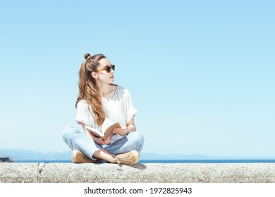 Pretty woman sitting on a stone bench with a book. Studying in a summer sunny day. - Powered by Shutterstock