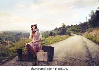 pretty woman sitting on the suitcases in a desert road