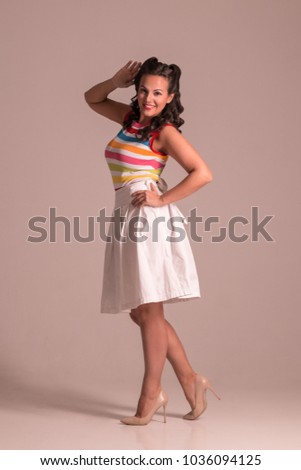 Pretty woman in skirt with hairdo poses in grey studio, pin up style, full body