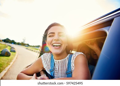 Pretty Woman In Speeding Car Smiles At Camera While Friends Laugh In Seat Behind Her