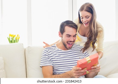 Pretty woman surprising her boyfriend with gift at home in the living room - Powered by Shutterstock