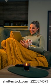 pretty woman with tablet sitting in chair at home reading book online watching a movie and drinking a hot coffee, tea - Shutterstock ID 2223574593