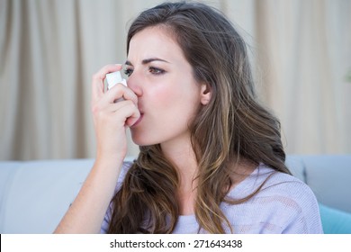 Pretty woman taking her inhaler at home at the living room