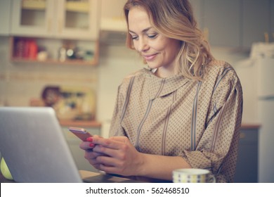 Pretty woman typing on her smart phone and using laptop at home.  - Powered by Shutterstock