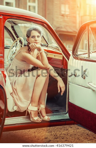 Pretty woman in veil  is sitting in\
the vintage car. Early summer morning on the\
background.