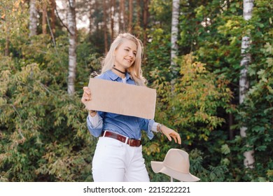 Pretty Woman Wait Passing Car In Forest Standing With Suitcase And Cardboard Poster On Roadside Of Highway. Blonde Lady Escape From City To Go Anywhere. Travelling, Auto Stop, Hitchhiking, Vacations.