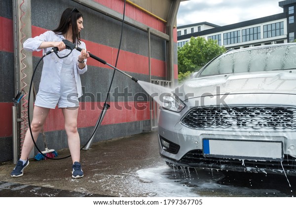 Pretty woman washing 
and car cleaning with foam and pressured water. Concept for
cleaning or care car. 