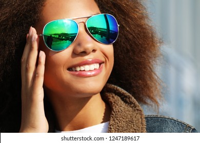  pretty woman wearing sunglasses with perfect teeth and dark clean skin having rest outdoors, smiling after received good positive news. Beautiful young dark-skinned female enjoy nature.