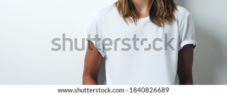 Pretty woman in white blank t-shirt, empty wall, studio close-up. Wide screen, panoramic
