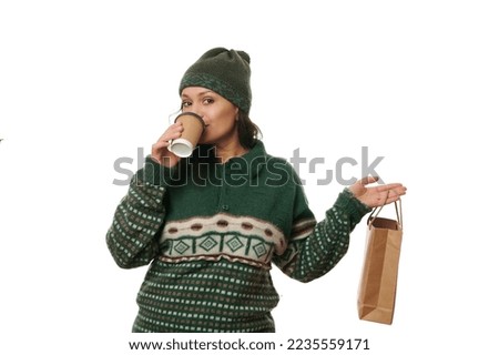 Pretty woman in woolen sweater and hat, drinking hot tea or coffee from a paper cup, holding a disposable eco bag with fresh delivered food, isolated over white background with free advertising space