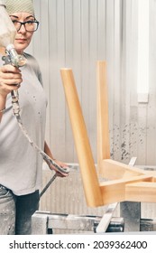 Pretty Woman Worker Paints Wooden Chair Base In Transparent Varnish With Spray Gun On Rack Support In Contemporary Spraying Booth Close View