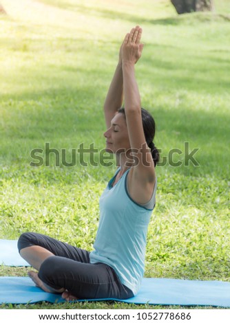 Pretty women Caucasian middle-aged women are practicing meditation And the body balance with yoga pose on green lawn in the shady park.