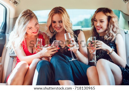 Pretty women having party in a limousine car, drinking champagne and use smartphone.