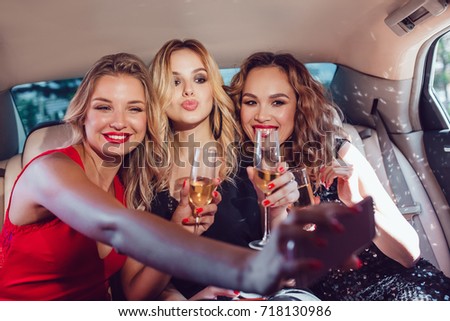 Pretty women having party in a limousine car, drinking champagne and make selfie.