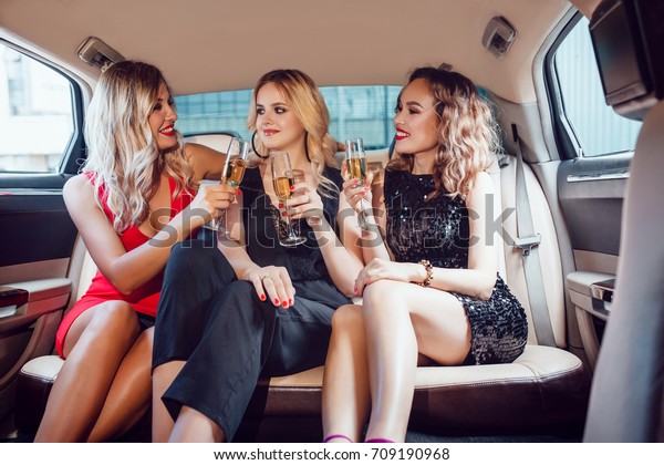Pretty women having party in a limousine car
and drinking champagne.