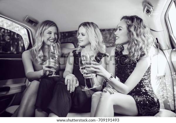 Pretty women having party in a limousine car\
and drinking champagne.