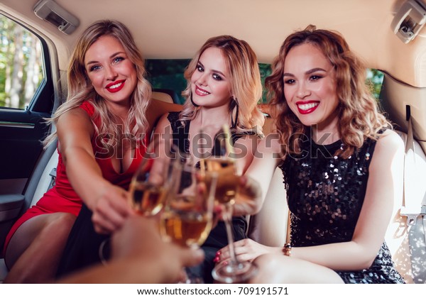 Pretty women having party in a limousine car\
and drinking champagne.