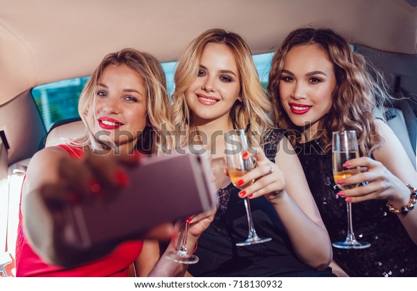 Pretty women having party in a limousine car,\
drinking champagne and make\
selfie.