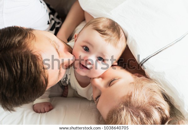 ベッドに入った綺麗な家族 両親は赤ちゃんにキスをする の写真素材 今すぐ編集