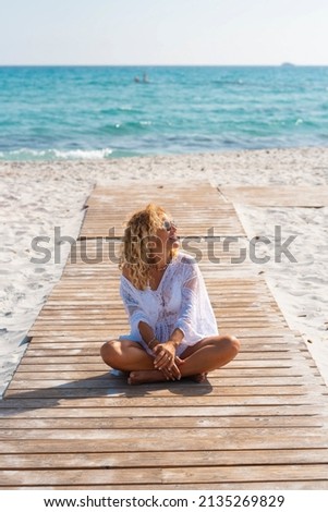 Pretty young adult tourist siting alone on the wooden pier with blue ocean and sky in background and sandy beach around. People and summer holiday vacation leisure concept lifestyle