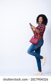 Pretty Young African Lady Looking Excited And Happy Using Her Phone, Carrying A Handbag, Standing Sideways