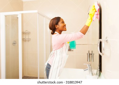 Pretty Young African Woman Wiping Bathroom Mirror At Home