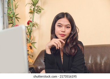 A pretty and young asian entrepreneur working on her laptop while looking at the camera. A beautiful female professional wearing a black blazer. - Shutterstock ID 2173516195