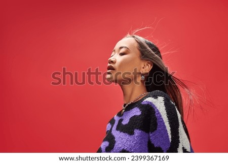 pretty young asian girl in vibrant sweater with animal print with heart shaped necklace on red