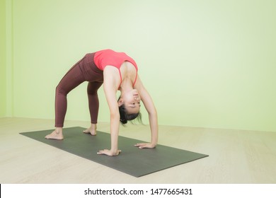 Pretty Young Asian Lady Doing Yoga Exercise On A Black Mat, Standing In Urdhva Dhanurasana Upward Bow, Chakrasana Wheel Posture, Indoor Shot.