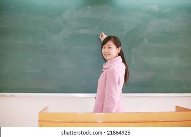 Pretty   Young Asian  Teacher In Front Of A Blackboard