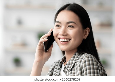 Pretty young asian woman chilling on couch at home, talking on cellphone, smiling and looking at copy space, closeup portrait. Happy chinese lady having phone conversation with girlfriend or lover - Powered by Shutterstock