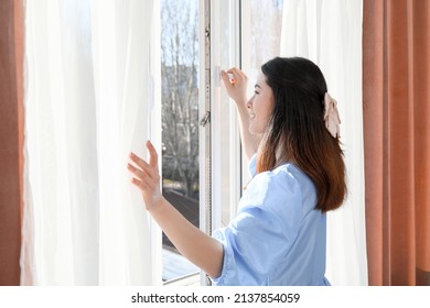 Pretty Young Asian Woman Opening Window In Room