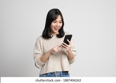 Pretty Young Asian Woman Using Smartphone Standing On Isolated White Background. She Texting On Cell Phone.