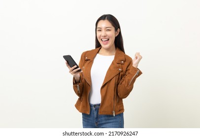 Pretty Young Asian Woman Using Smartphone Standing On Isolated White Background. She Texting On Cell Phone. Dressing With Jacket And Jean.