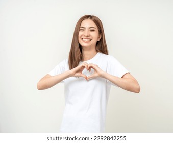 Pretty Young beautiful Asian woman standing and smiling showing heart sign isolated on white background. Lovely female wearing brown shirt feeling surprised and happy.