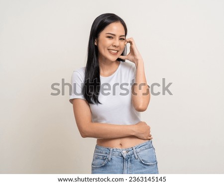 Pretty Young beautiful Asian woman standing smiling showing mini heart sign on cheek with isolated white background. Attractive Lovely Latin female wearing white shirt feeling surprised and happy.